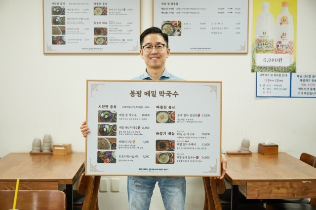 서울시 양천구에 위치한 ‘봉평 메밀 막국수’ 사장님이 바뀐 메뉴판을 들고 포즈를 취하고 있다. /우아한형제들